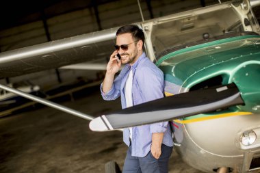 Hangarda uçak kontrol ve cep telefonuyla genç yakışıklı genç pilot
