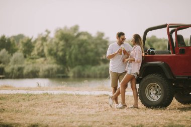 Genç kadın ve adam arabanın yakınında açık yaz gününde eğleniyor