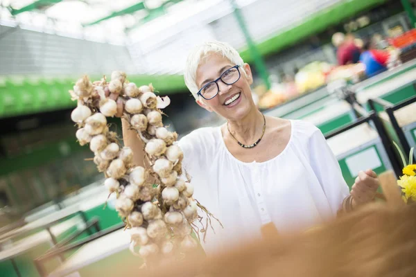 stock image Portrait of senior woman buying lot of garlic on market