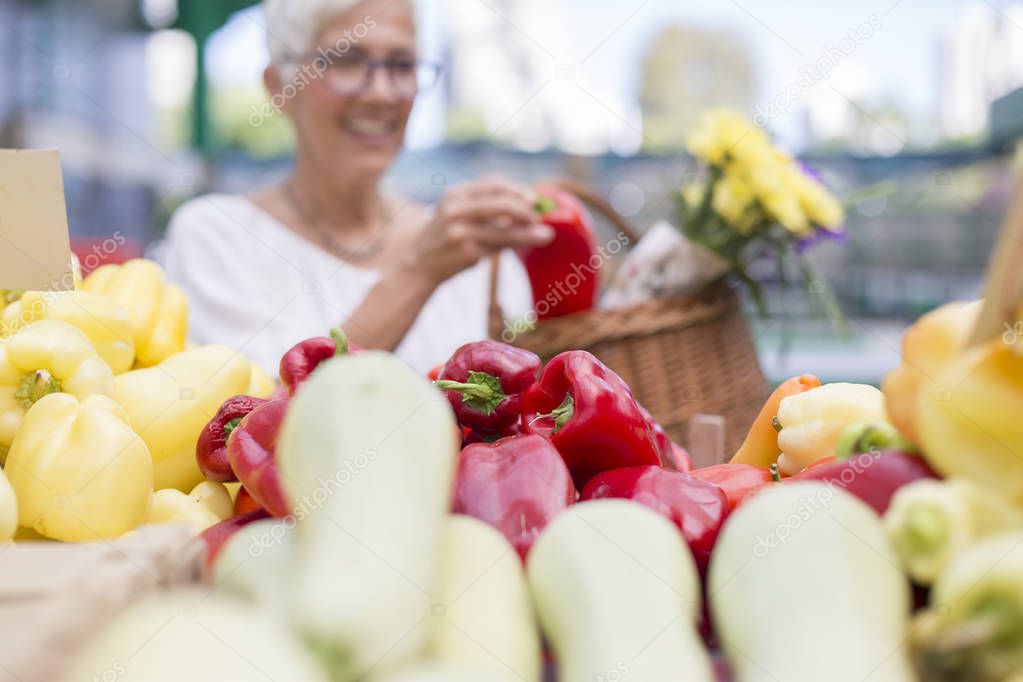 Portrait of good-looking senior woman wearing glasses buys pepper on market