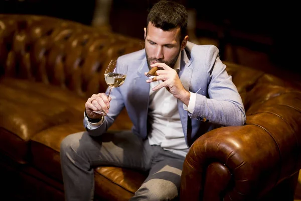 Богатый Молодой Бизнесмен Пробует Белое Вино Курит Сигары — стоковое фото