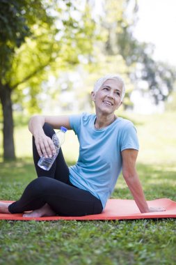 Çimenlerin üzerinde otururken egzersiz sonra rahatlatıcı gülümseyen kadın kıdemli portresi