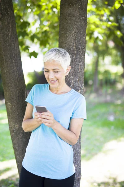 公園で携帯電話を使用してスポーティな年配の女性の肖像画 — ストック写真