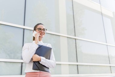 Smartphone kullanarak ve belgeler açık havada tutan başarılı genç iş kadını portresi.