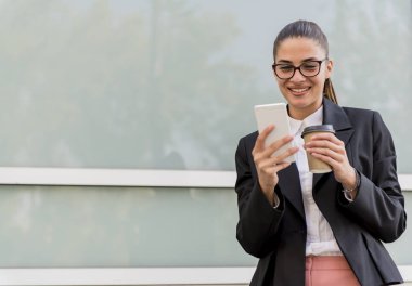 Cep telefonu kullaranarak ve açık bir kopma üzerinde kahve içme genç işkadını portresi