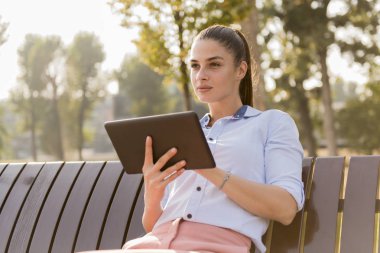 Bankta otururken tablet kullanan genç güzel kız