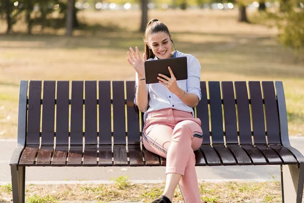 坐在长凳上的年轻女子在公园和听音乐在平板电脑上 — 图库照片
