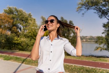 Nehir kenarındaki parkta cep telefonu kullanan genç kadın portresi