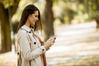 Cep telefonu sonbahar parkta güzel günde kullanan mutlu genç kadın