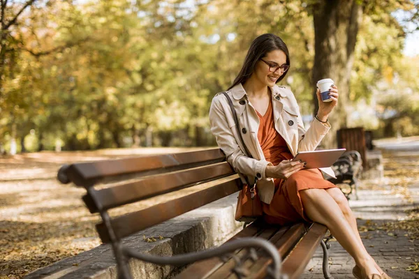 Vrouw Drinkt Koffie Zittend Bankje Park Tijdens Herfstweer Tablet Gebruiken — Stockfoto