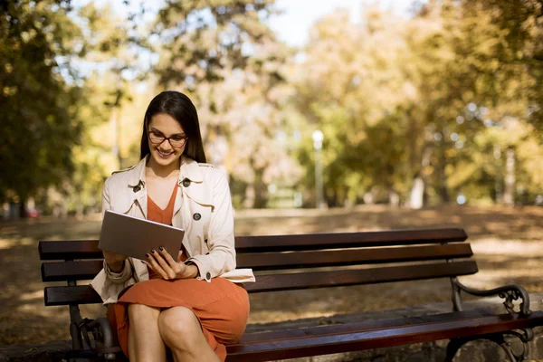 妇女坐在公园长凳在秋季天气使用平板电脑和检查社交媒体 — 图库照片