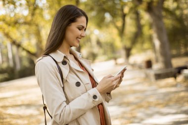 Cep telefonu sonbahar parkta güzel günde kullanan mutlu genç kadın