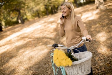 Sonbahar parkta smartphone kullanarak Bisiklet çarklı genç kadınla