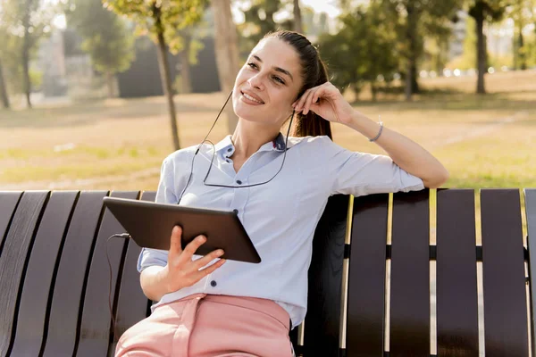 Mujer Joven Sentada Banco Parque Escuchar Música Una Tableta — Foto de Stock