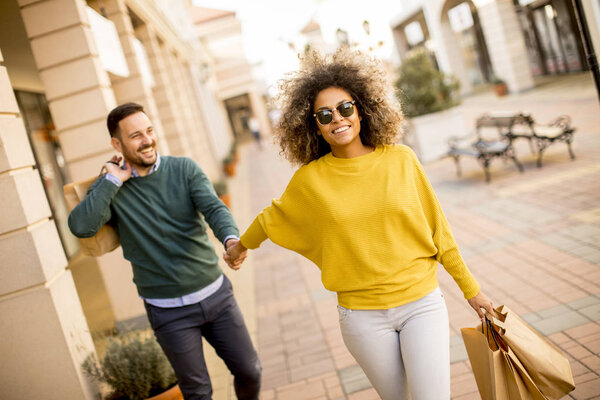 Young and cheerfull couple walking along street with shopping bags