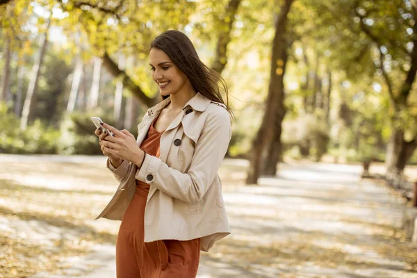 Cep telefonu sonbahar parkta güzel günde kullanan mutlu genç kadın