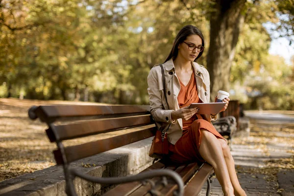 女性が飲むコーヒーと秋の天気の時に公園のベンチに座って タブレット を使用して ソーシャル メディアをチェック — ストック写真