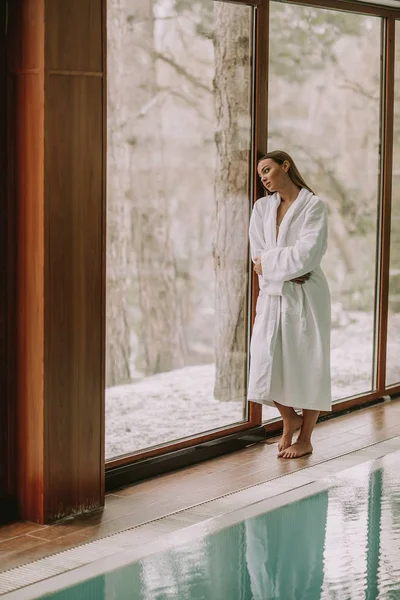 Pretty young woman in bathrobe standing by swimming pool