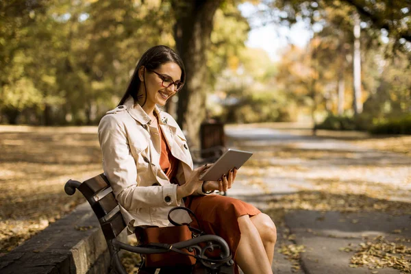 妇女坐在公园长凳在秋季天气使用平板电脑和检查社交媒体 — 图库照片
