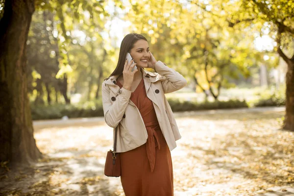 美しい日に秋の公園で携帯電話を使用して幸せな若い女 — ストック写真