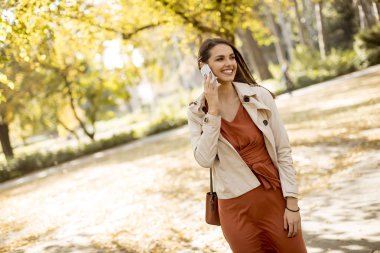 Cep telefonu sonbahar parkta güzel günde kullanan mutlu genç kadın