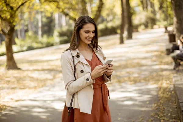 愉快的年轻妇女使用手机在秋季公园在美丽的一天 — 图库照片