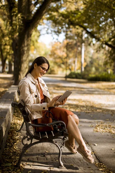 女性は秋の天気を使用してタブレット の間に公園のベンチに座っているとソーシャル メディアをチェック — ストック写真
