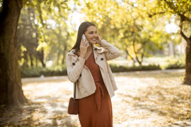 Cep telefonu sonbahar parkta güzel günde kullanan mutlu genç kadın