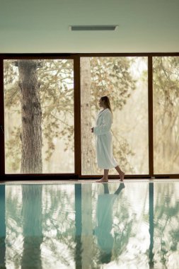 Genç ve güzel kadın bornoz ayakta yüzme havuzu tarafından