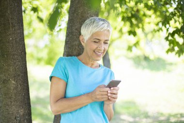 Cep telefonuyla parkta güneşli günde sportif kadın kıdemli portresi