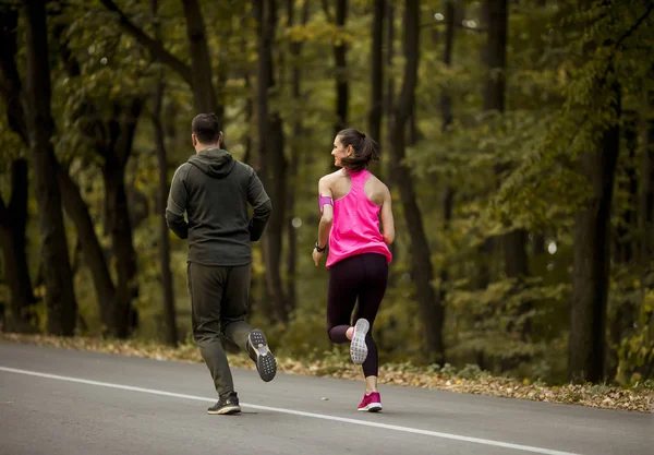 Athletic couple running together on the forest trail in autumn
