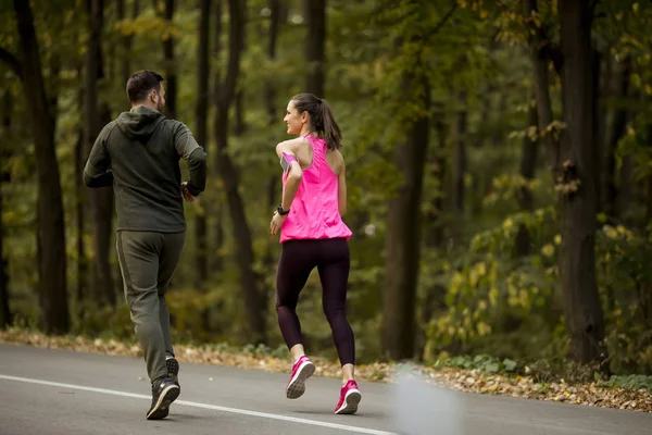 Athletic couple running together on the forest trail in autumn