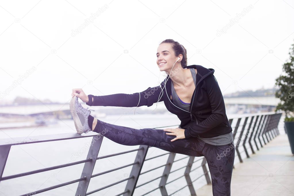 Pretty young woman with earphones stretching during sport training in urban enviroment