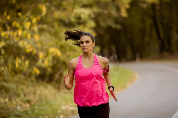 Young fitness woman running at forest trail in golden autumn