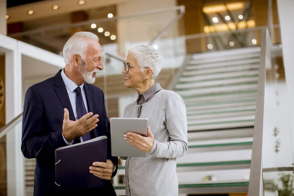 Senior business people standing in office with tablet and paper documents