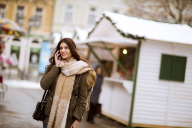 Telefonunuzun parkta soğuk kış gününde gülümseyen genç kadın portresi