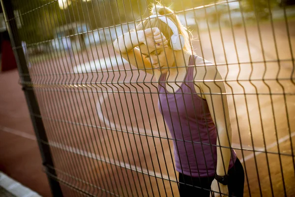 裁判所の金属フェンスで休んでいるスポーティな若い女性 — ストック写真