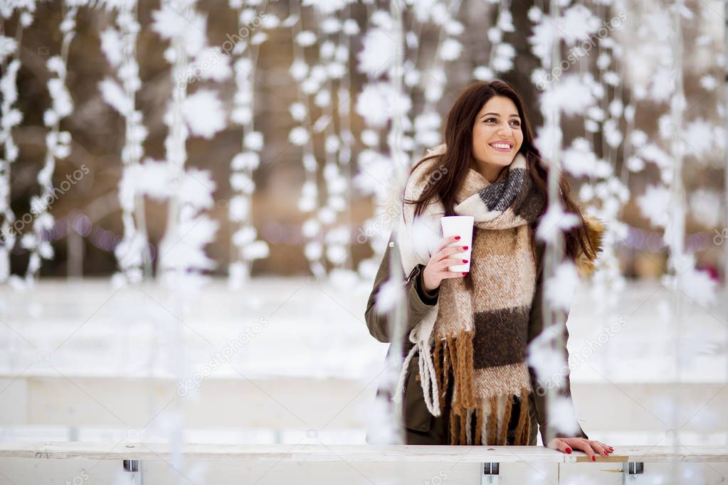 Portrait of young woman in a snow park drinks tea