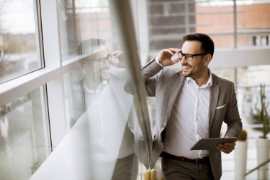 Modern ofis ayakta ve tablet kullanarak takım elbise giymiş mutlu işadamı
