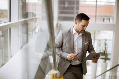 Modern ofis ayakta ve tablet kullanarak takım elbise giymiş mutlu işadamı
