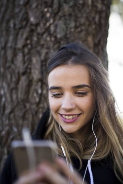 Hatta bir akıllı telefon ağacına üzerinden kablosuz kulaklık ile müzik dinleme bir mutlu kız portresi