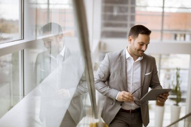 Modern ofis ayakta ve tablet kullanarak takım elbise giymiş mutlu işadamı