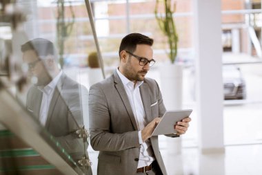 Modern ofis ayakta ve tablet kullanarak takım elbise giymiş mutlu işadamı