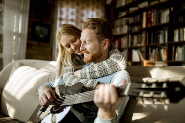 Adam kanepede genç güzel kadını için akustik gitar çalmak