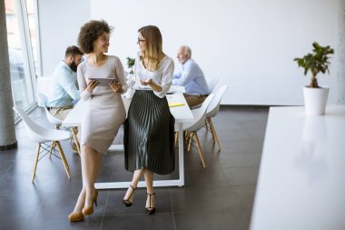 Bir tablet ofis ve masa başında çalışan diğer iş adamları ile iki genç iş kadınları