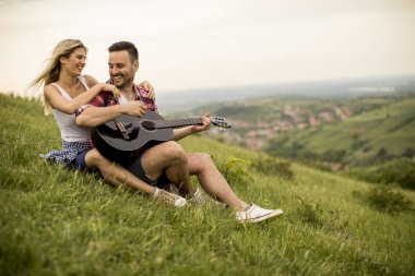 Sevgi dolu adam kız arkadaşı ve gitar çalmak ile çimlerde oturuyor