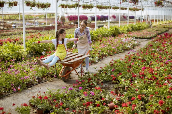 Two playful florist enjoying work while one of them riding in the cart at the greenhouse