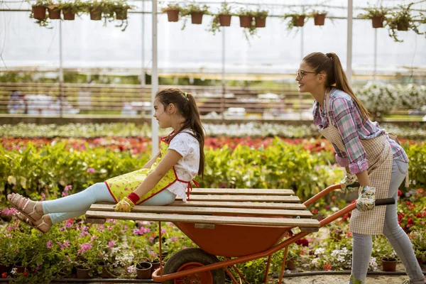 Two playful florist enjoying work while one of them riding in the cart at the greenhouse