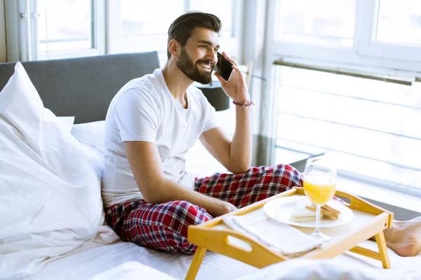 Joven Guapo Desayunando Cama Usando Teléfono Móvil — Foto de Stock