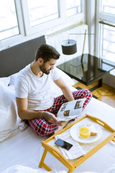 Молодий Бородатий Чоловік Снідає Ліжку Читає Журнал Кімнаті — стокове фото